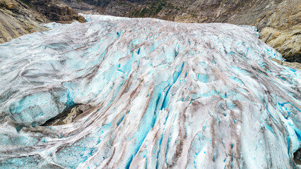 A massive blue glacier flows between rocky mountain slopes, showcasing deep crevasses and ancient ice. This landscape represents climate change, environmental preservation, and geological power. © JULIA