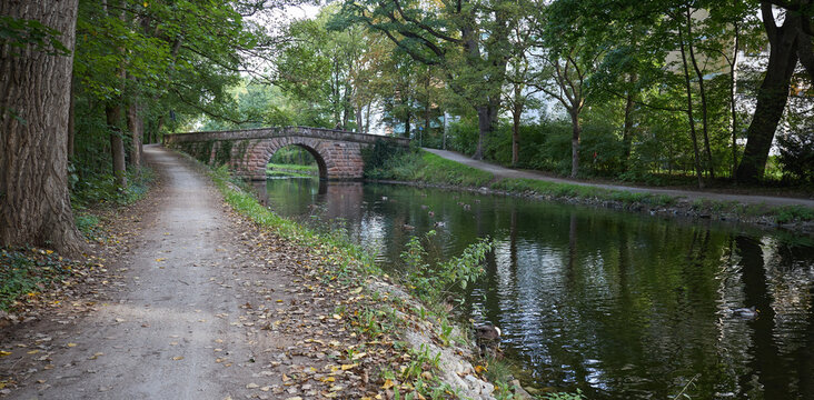 Scenic stone arch bridge over a calm canal path surrounded by lush green trees in autumn