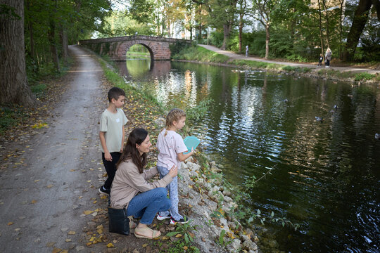 A mother and her two children standing by a scenic canal path in a park during the autumn season