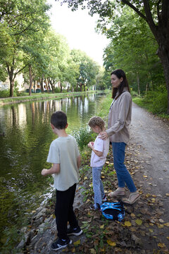 A mother and her two children standing by a calm canal on a peaceful autumn afternoon in nature