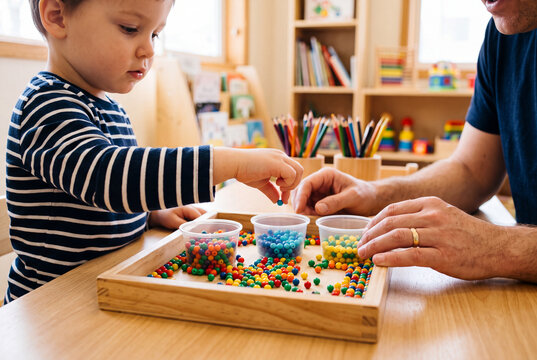 Child Development and Fine Motor Skills Activity with Father or Therapist Sorting Colorful Beads in Early Learning Classroom