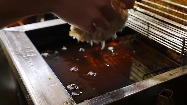 The culinary process involves placing breaded meat portions into hot cooking oil inside a deep fryer within a restaurant kitchen setup