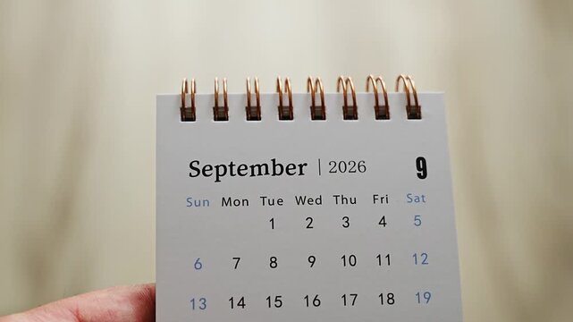 Hand holding desk calendar showing September 2026 page with dates and weekday columns on neutral background