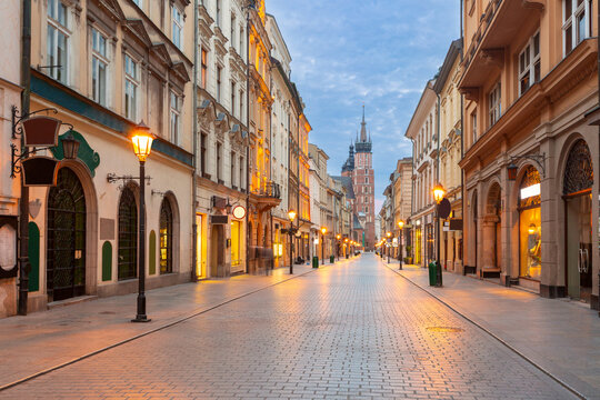 Historic street in central Krakow with illuminated buildings and St Mary s Basilica in the background during early morning.