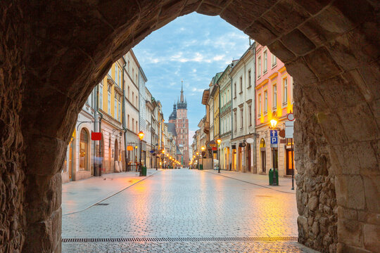 Historic street in central Krakow with illuminated buildings and St Mary s Basilica in the background during early morning.