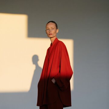 Contemporary studio portrait of a woman in a red coat with strong shadow and geometric light for fashion portrait with minimalist composition and dramatic contrast