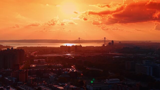 Beautiful orange light colors the scenery at sunset time. Flight above New York City, USA. The Verrazzano-Narrows Bridge in the backdrop.