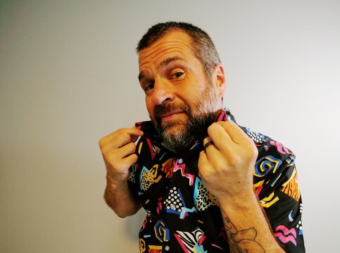 Middle aged man in 1980s graphic pattern shirt neon sunglasses and fanny pack posing humorously trying to look cool on neutral studio background