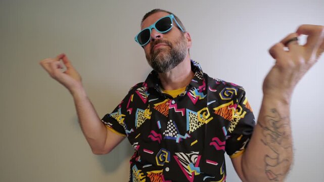 Middle aged man in 1980s graphic pattern shirt neon sunglasses and fanny pack posing humorously trying to look cool on neutral studio background