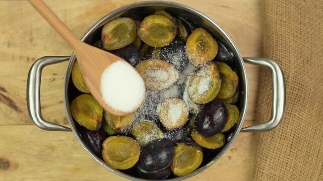 Adding sugar to plums in a pot to make jam 