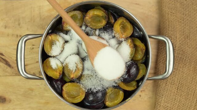 Adding more sugar  to plums in a pot to make jam, top view 	
