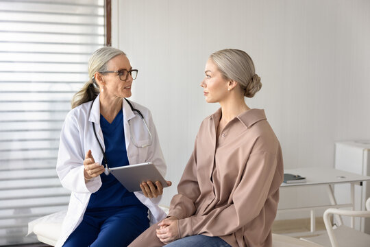 Female general practitioner holding digital tablet, discussing checkup results with woman patient during appointment at hospital office. Healthcare services, professional consultation, medical advice