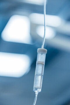 IV drip chamber close up with saline solution dripping, intravenous infusion in hospital operating room, blue medical background with copy space