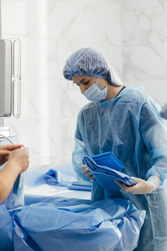 Surgical nurse in sterile gown preparing ophthalmic surgery system and tubing before eye operation, medical team in ophthalmology operating room