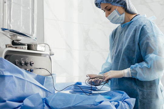 Female surgical nurse connecting instrument cable to ophthalmic surgery machine before eye operation in modern ophthalmology operating room