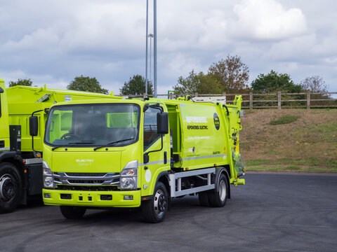 Birmingham, UK - September 17th September: green electric refuse truck parked on paved lot under cloudy sky, showing cab, windshield, side mirrors, and rear lift mechanism
