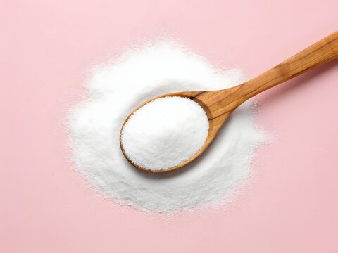 Wooden spoon filled with powdered sugar on pink studio background for food packaging design