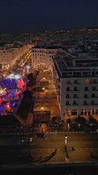 THESSALONIKI, GREECE - DECEMBER 31, 2024: Vertical aerial video panning across a glowing central city square filled with colorful lights and crowds celebrating New Year's Eve at night.