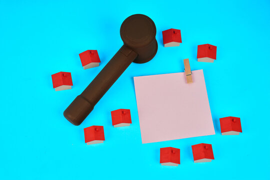 A judge gavel surrounded by miniature houses and a blank document represents property law housing disputes and real estate agreements.
