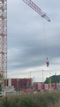 Construction crane operation, Urban building site activity, Heavy machinery working on developing urban infrastructure under cloudy weather. Vertical user generated content.