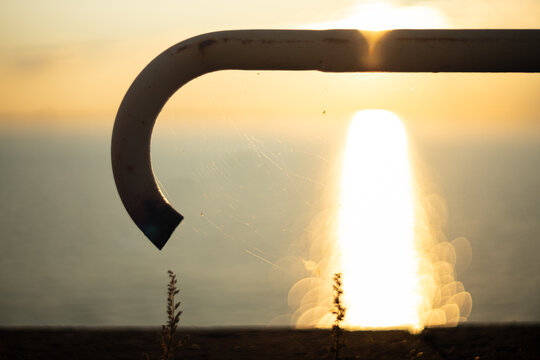 Silhouetted metal hook framing golden sunrise over ocean horizon