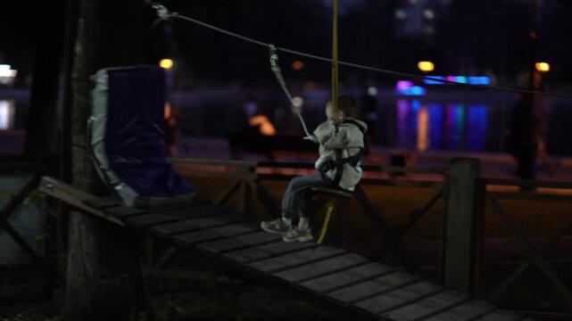 Young boy riding a zip line in an outdoor rope park, enjoying an exciting adventure at dusk tonight.