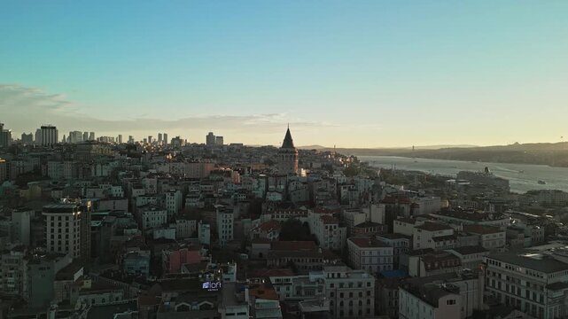 Turkey, Istanbul 06 10 2025: 4K drone video moving backward away from Galata Tower backlit by sunrise with Bosphorus Bridge in background.