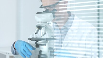Scientist in a white lab coat and blue gloves examining samples using a modern microscope,...
