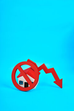 A miniature house behind a prohibition symbol and downward arrow represents housing restrictions and declining property market conditions.
