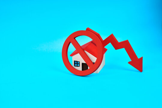 A prohibition symbol covering a miniature house beside a downward arrow represents falling property values and housing market decline.
