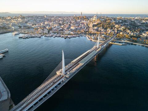 Turkey, Istanbul 06 10 2025: Diagonal drone photo of Halic Golden Horn Metro Bridge with Eminonu ferry terminal, Fatih area, and Suleymaniye Mosque on hill during sunrise.