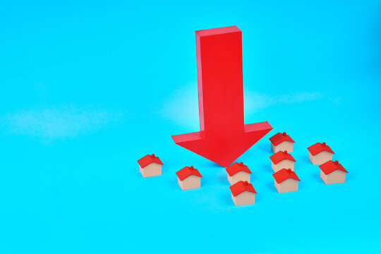 A large downward arrow surrounded by miniature houses represents falling property values and a declining real estate market.
