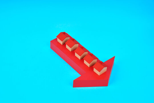 Miniature houses placed on a downward arrow represent falling home prices and declining real estate market values.
