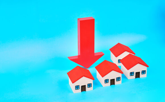 A large downward arrow above miniature houses represents a property market downturn and declining housing values.
