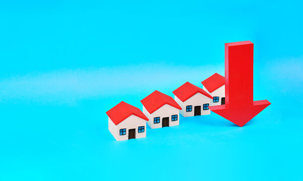 Miniature houses beneath a large downward arrow represent decreasing property values and real estate market contraction.
