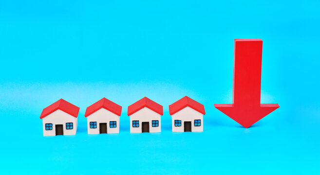 A row of miniature houses beside a downward arrow represents falling real estate values and declining property prices.
