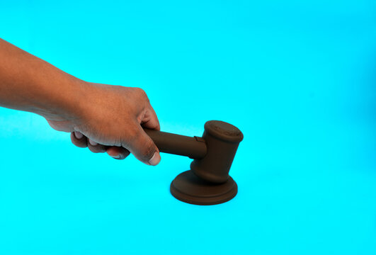 A hand holding a judge gavel above its base represents court decisions legal authority and justice enforcement.
