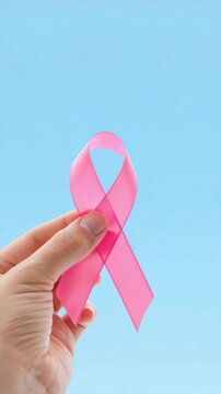 Pink ribbon held against blue background, breast cancer awareness, oncology support, early detection, women health campaign, prevention education, October awareness