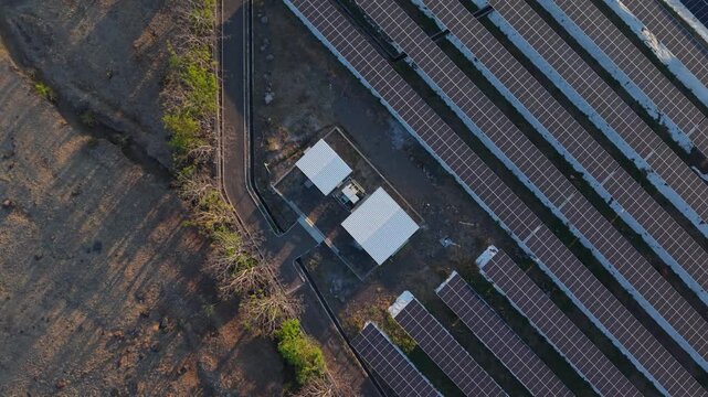 Solar panels stretch across barren land. Tiny structure sits amid the rows. Sunlight glints off each dark surface. Dry earth contrasts with clean energy. Nature and innovation coexist here