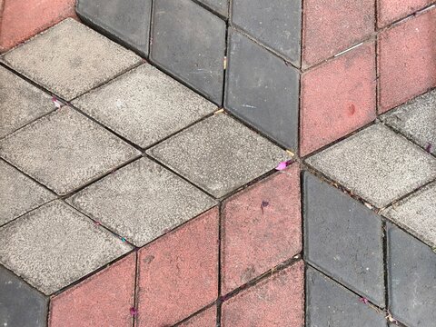 Top view of geometric interlocking concrete paving blocks in contrasting red, grey, and dark charcoal colors. Textured surface pattern for outdoor flooring, sidewalk, or driveway background