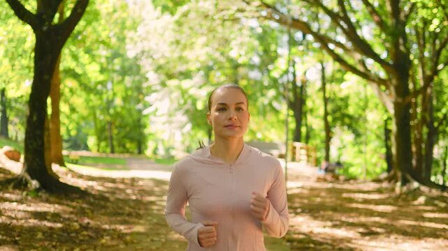 Woman, running and calm in nature with fitness, jogging or moderate pace outdoor. Front view, athlete or runner with earphones, trail path and cardio training in forest.