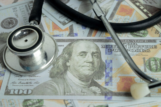 Close up of a stethoscope resting on scattered US dollar bills. Concept of expensive healthcare costs, medical insurance, hospital fees, financial health, and investment in medical business.