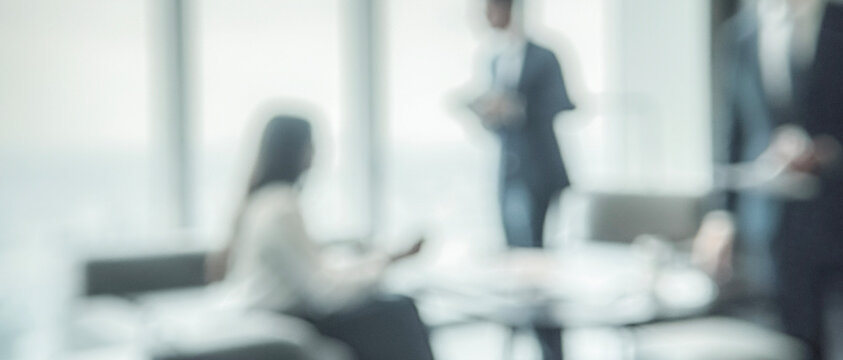A blurred image depicting a business meeting atmosphere, featuring professionals in formal attire engaged in discussions, enhancing the corporate environment.