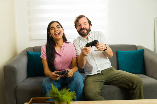 Cheerful couple relaxing on sofa, playing video games at home, laughing and having fun together during date