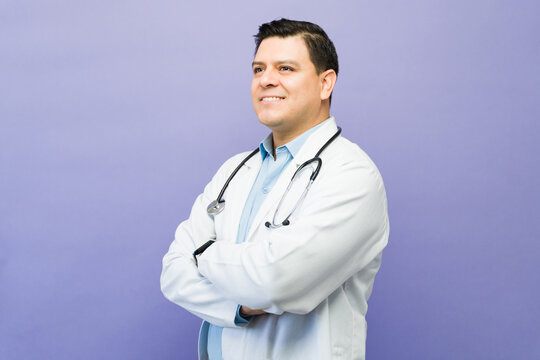 Male doctor smiling, confidently looking away on a plain background, representing healthcare, wellness, and medical expertise
