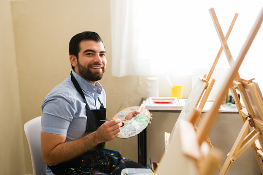 Cheerful man enjoying art class, painting on canvas with brush and palette, developing creativity and hobbies