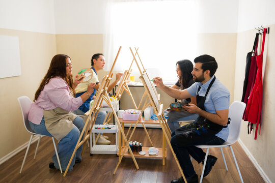 Group of adult students painting on canvas with easels during art class, learning new creative skills