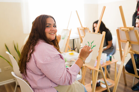 Portrait of a woman enjoying art class painting on canvas, learning creative skills and having fun in a workshop