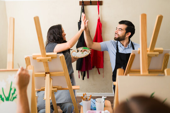 Students enjoying painting class, celebrating success with high five, learning creative art skills together