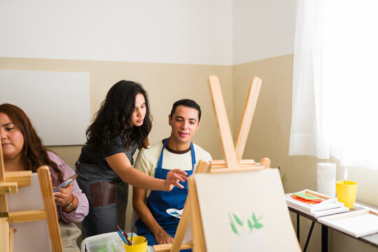 Teacher helping student during adult art class, learning painting techniques and developing creative skills